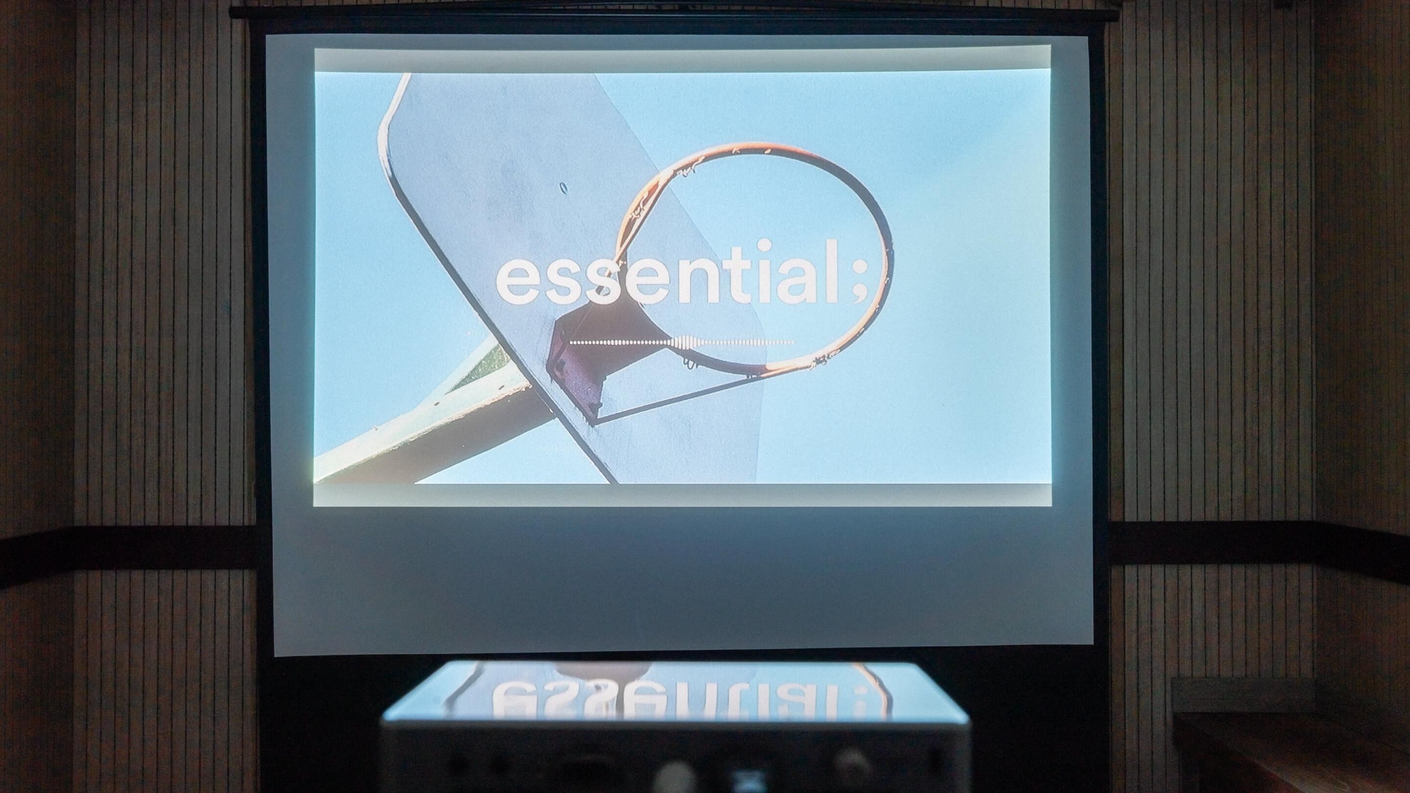 Uno schermo di proiezione mostra la parola 'essential' con un canestro da basket e una retina.