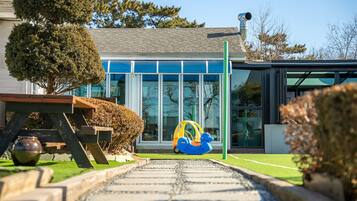 Een modern huis met een geplaveid pad dat leidt naar een glazen deur, een kleine tuin met een bankje, en een blauwe speelauto.