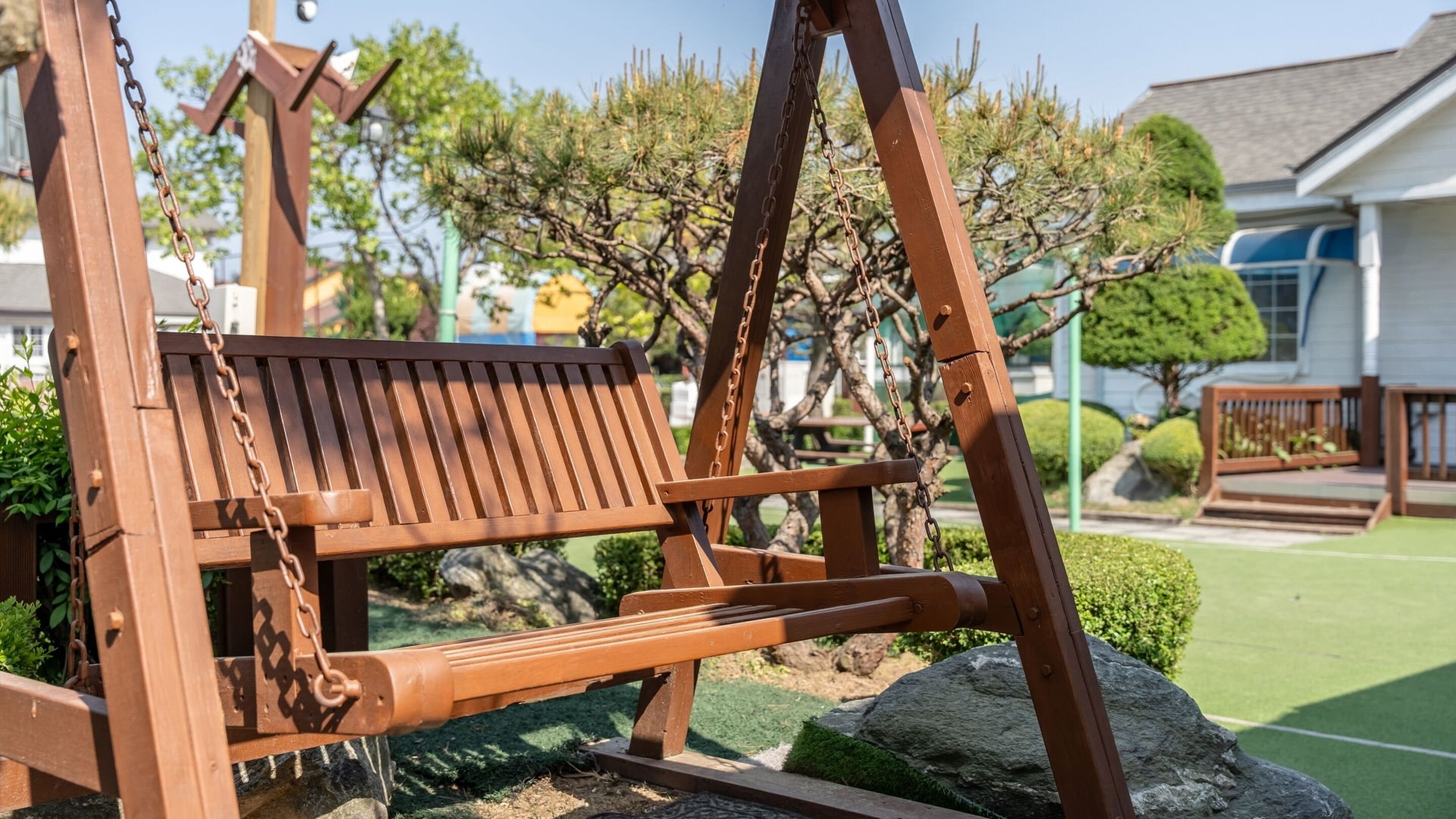 Un columpio de madera en un jardín, con una casa al fondo.