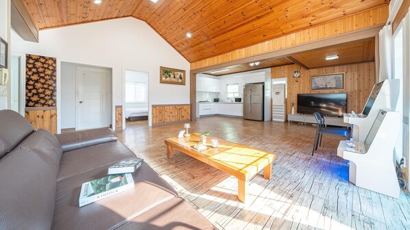A spacious living area with a wooden ceiling, a sofa, a coffee table, and a TV. - Daebudo Olive Poolvilla Pension (Ansan)