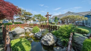 Un jardín japonés tradicional con un estanque de carpas, un puente de madera y una valla de madera.