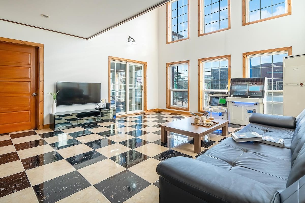 A spacious living room with a checkered floor, a large flat-screen TV, a leather sofa, and a coffee table.