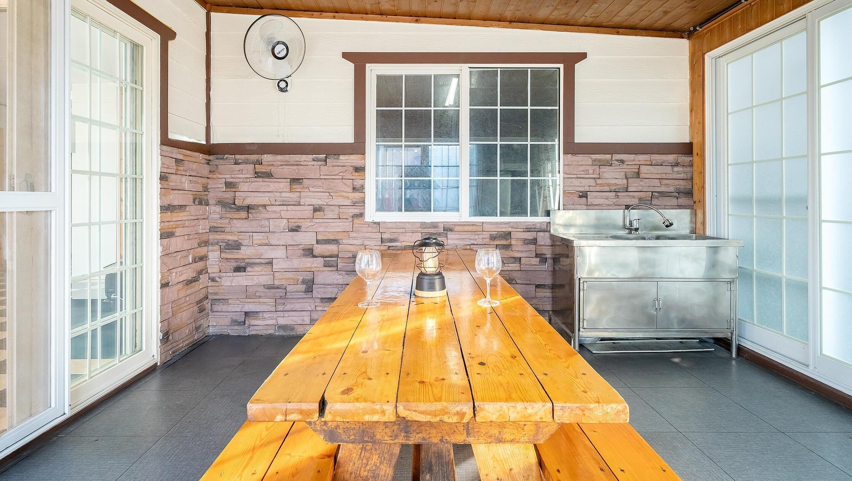 Una mesa de picnic de madera con dos copas de vino, un muro de piedra, una ventana y un lavamanos.