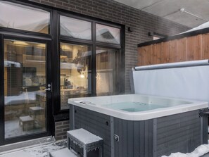 Un bain à remous situé à l’extérieur d’un bâtiment, avec une terrasse en bois et une porte en verre.