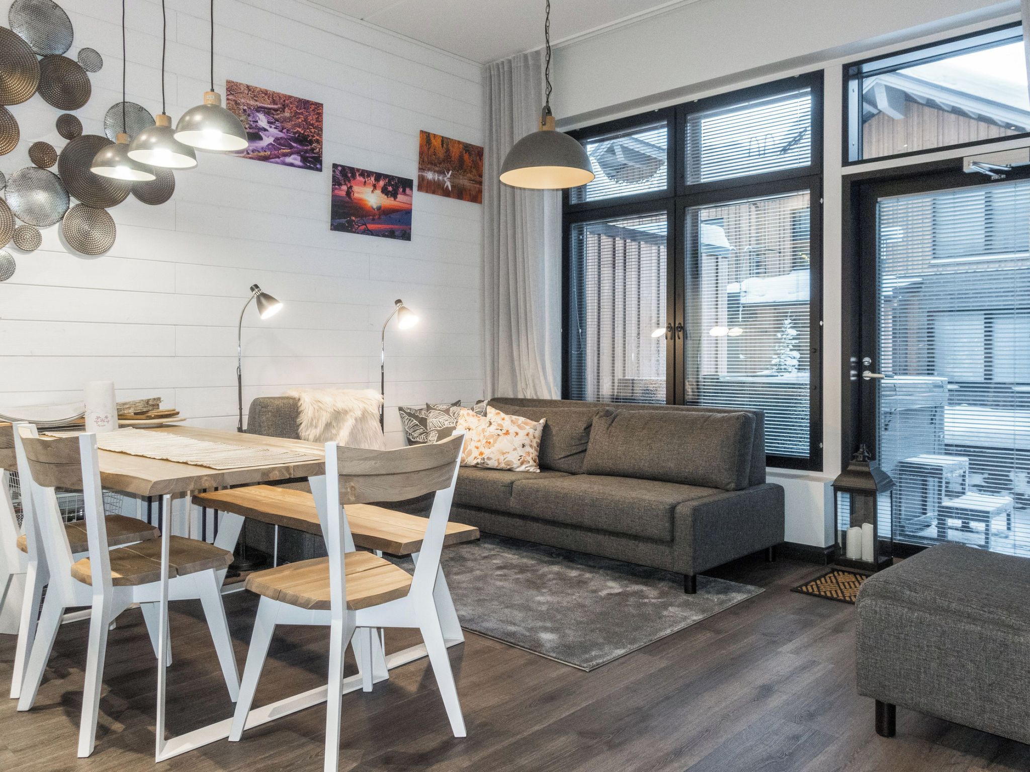 A modern living room with a dining area, large windows, and artwork on the walls.