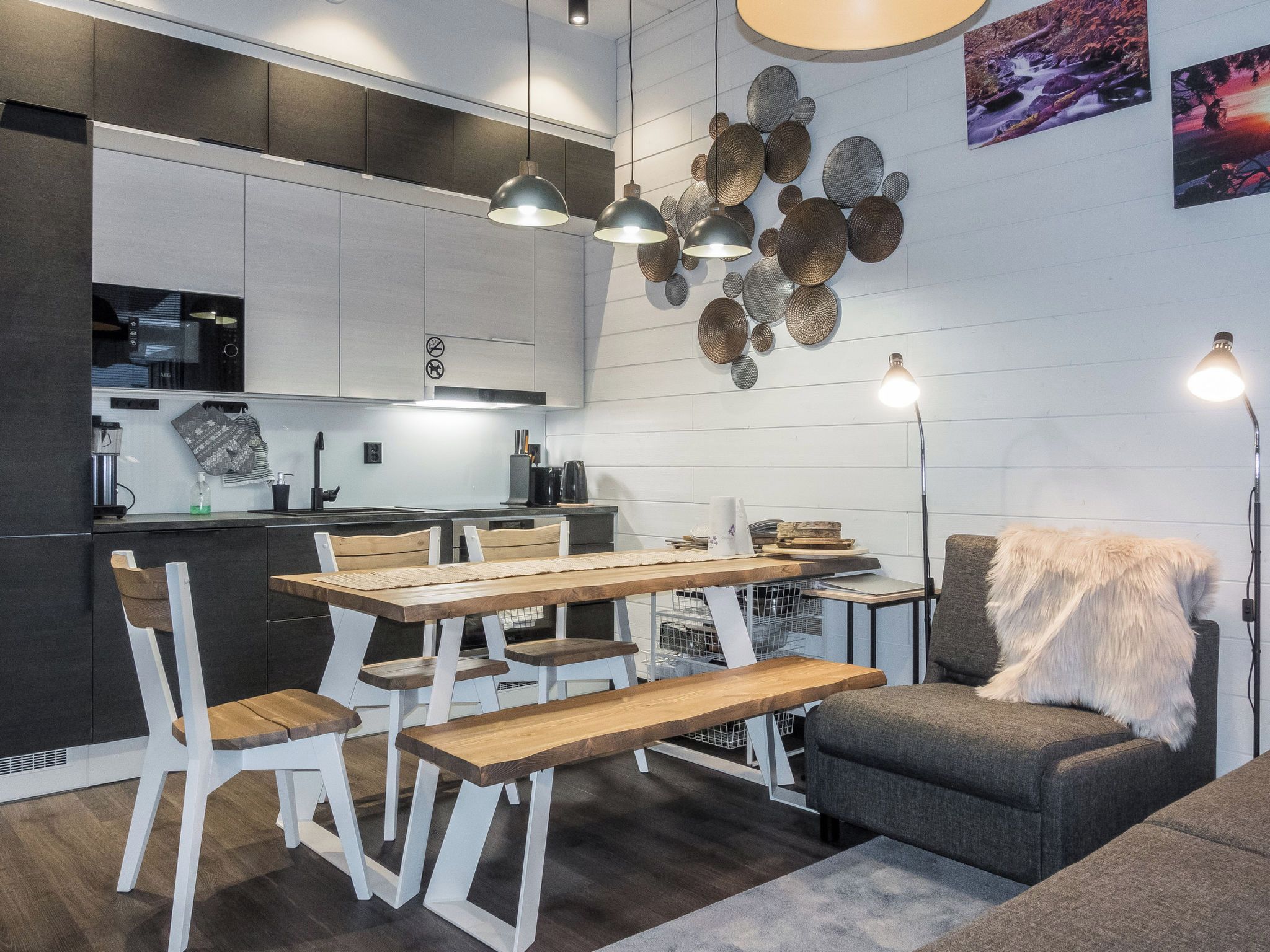 Une cuisine moderne avec un coin repas, comprenant une table en bois, des chaises blanches et des luminaires suspendus.