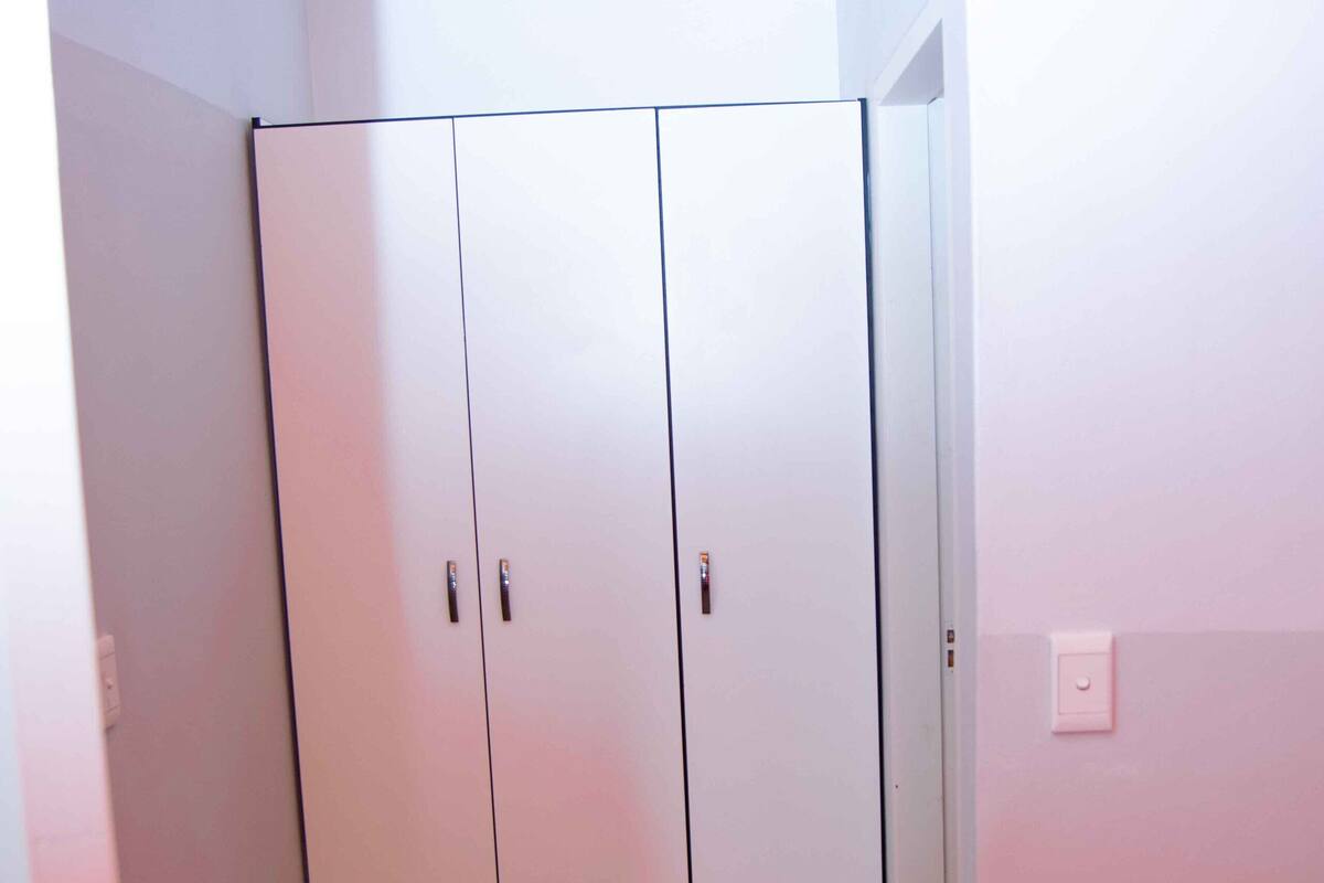 Una habitación con un armario blanco, suelo de baldosas y pared blanca.