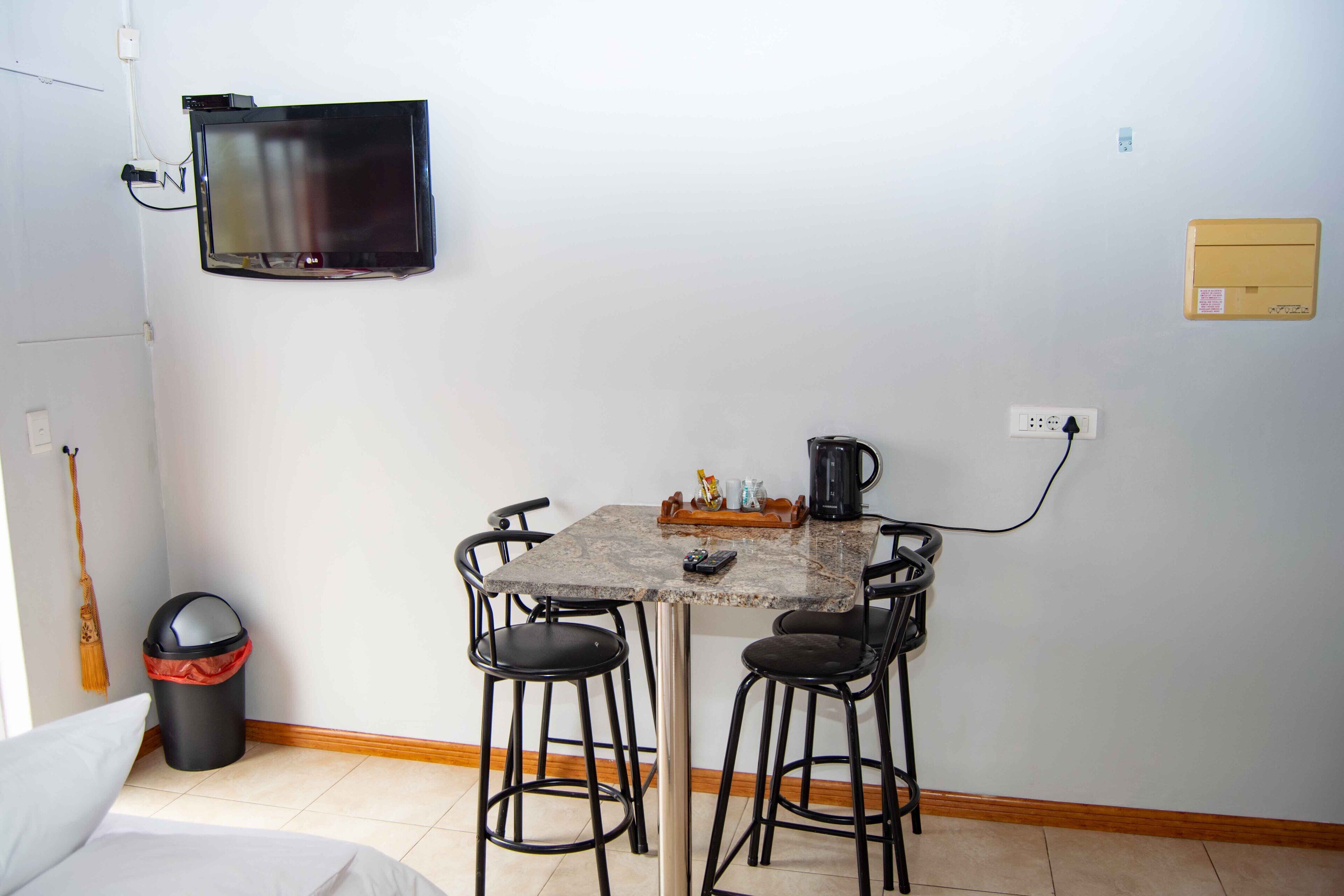 En liten matplats med ett bord, två stolar, en tv som är monterad på väggen och en papperskorg.