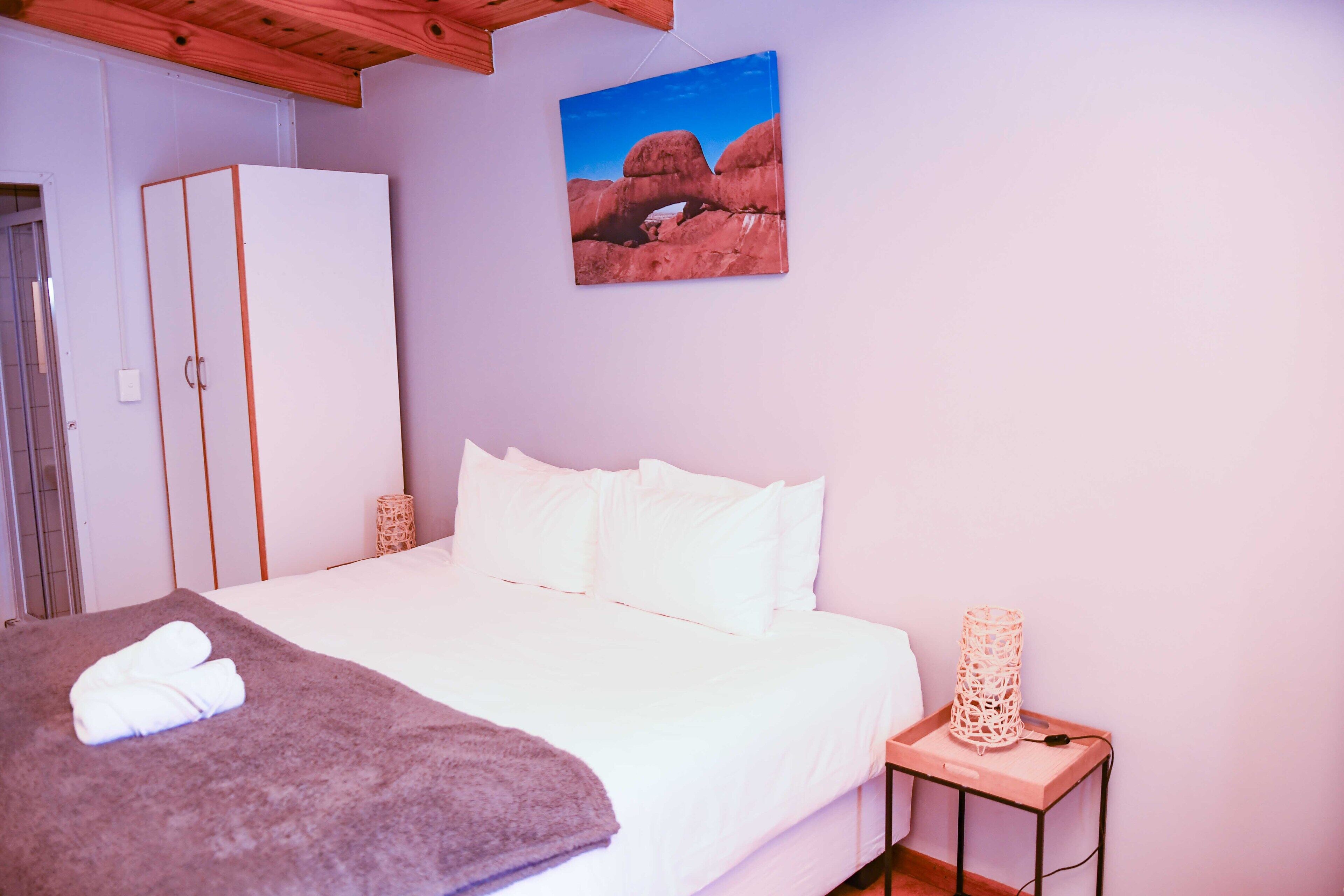Een slaapkamer met een bed, een witte kledingkast en een schilderij van rode rotsformaties.