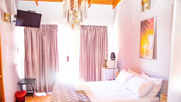 Een hotelkamer met een bed, gordijnen, een televisie, een kroonluchter en een schilderij aan de muur.