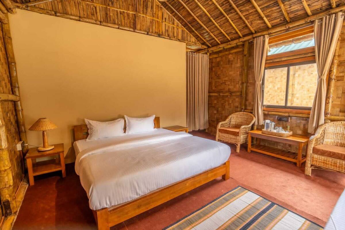 Een kamer met een groot bed, een nachtkastje, een rieten stoel en een raam met gordijnen.