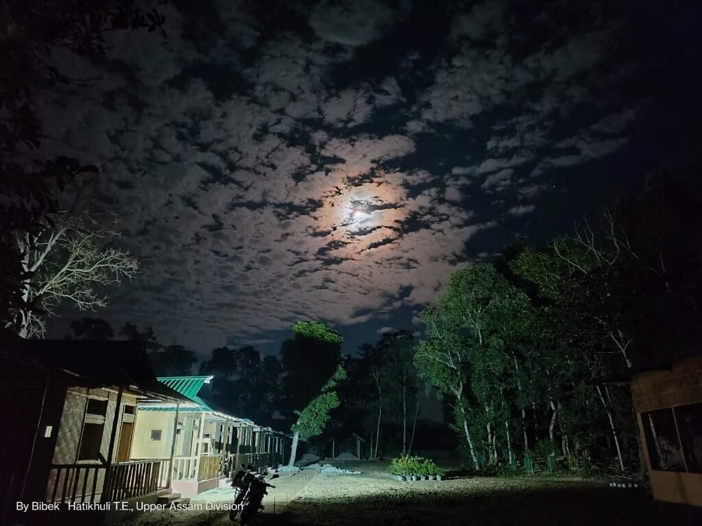 A night scene with a house and trees under a cloudy sky.