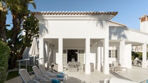 Un bâtiment blanc doté d’une piscine, de chaises longues et d’un patio couvert.