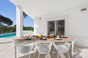 A dining table with white chairs, a pool, and a view of the landscape. - Villa Mirella - Varandas do Lago (Almancil)