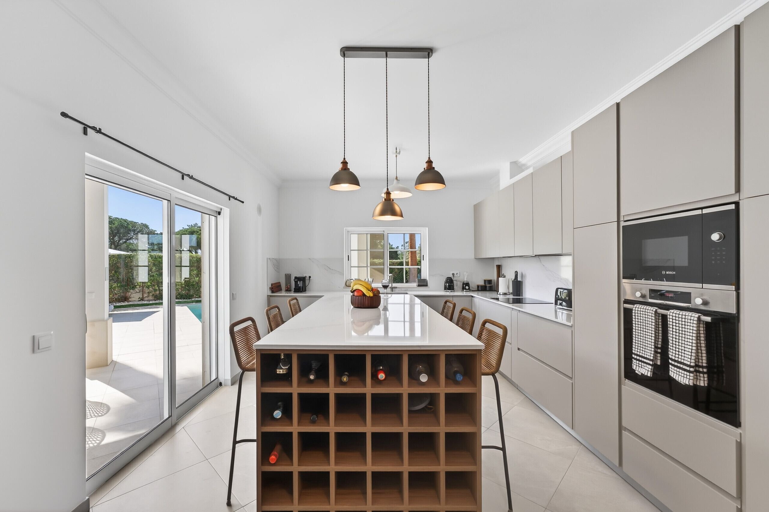 Eine moderne Küche mit einer zentralen Kochinsel, Weinkühlschrank und Blick ins Freie.