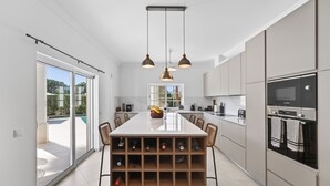 Une cuisine moderne dotée d’un îlot central, d’un espace de rangement pour les bouteilles de vin et offrant une vue sur l’extérieur.