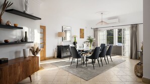 Une salle à manger moderne avec une table en verre, des chaises noires et un tapis gris. On y trouve des étagères ornées d’objets décoratifs et un buffet en bois.