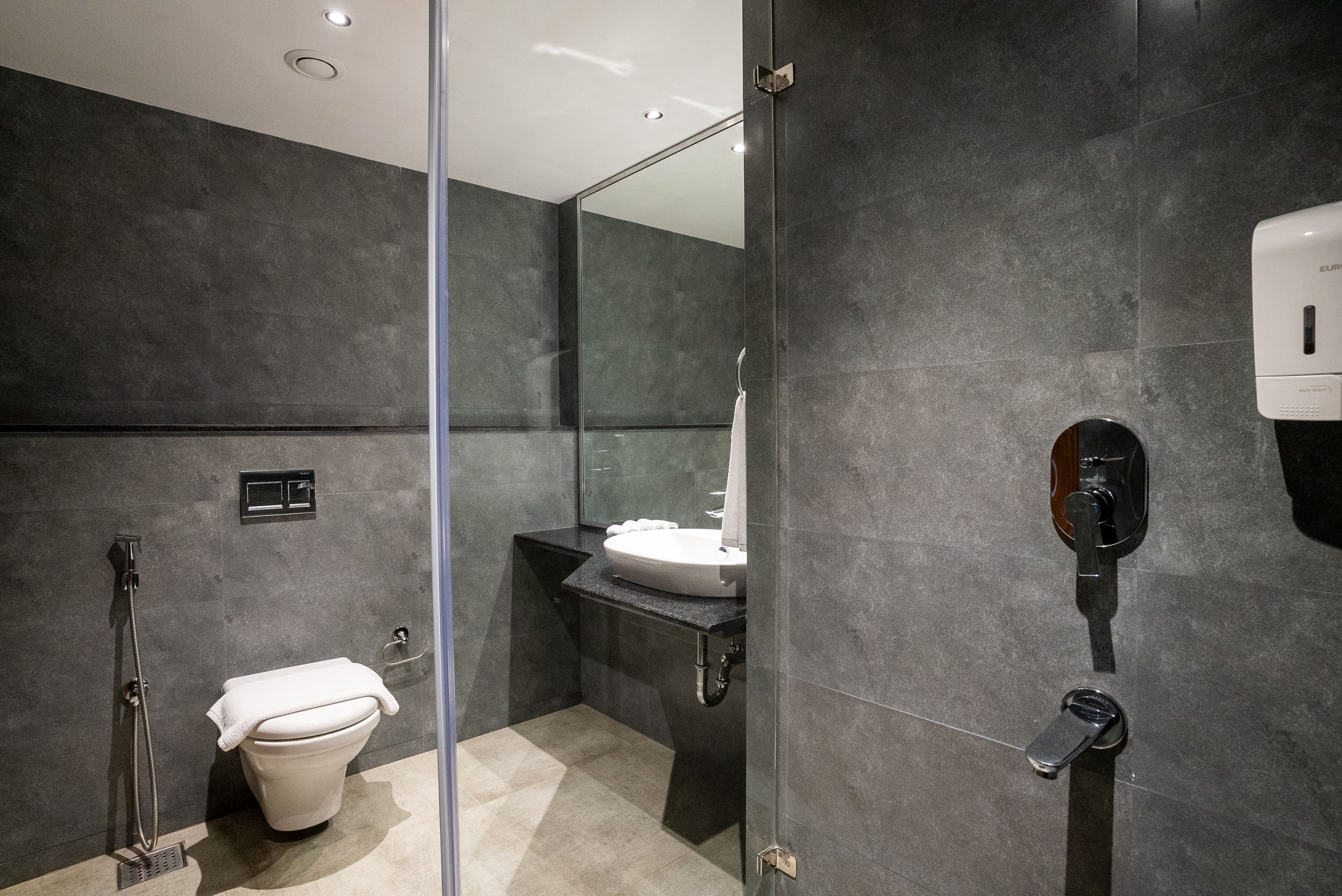 Un baño moderno con cabina de ducha de vidrio, inodoro blanco y lavamanos con dispensador de jabón.