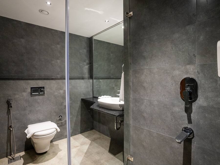 Un baño moderno con cabina de ducha de vidrio, inodoro blanco y lavamanos con dispensador de jabón.