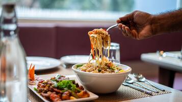 Een eettafel met een kom noodles, een bord roerbakgroenten en een waterfles.