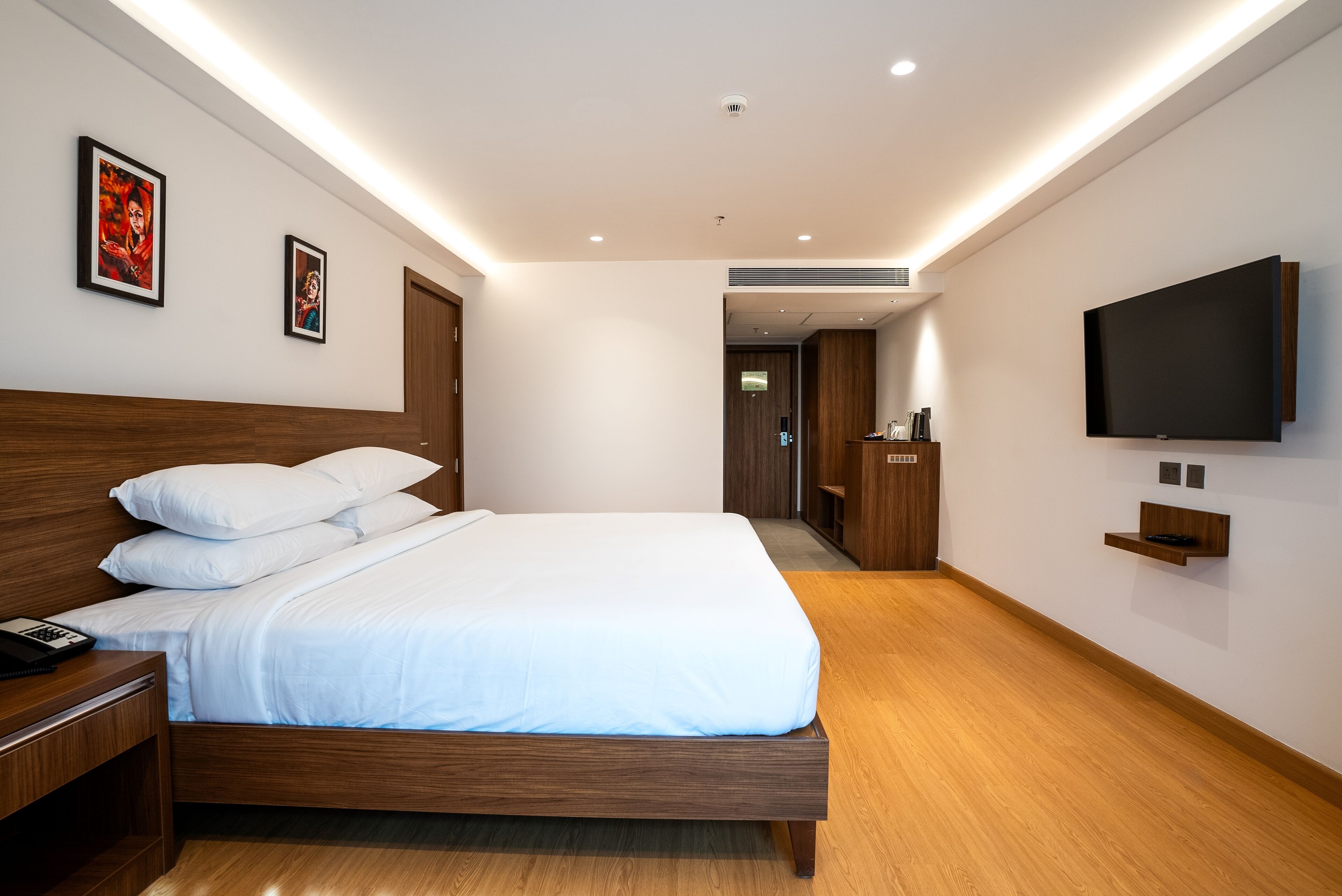 Una habitación de hotel moderna con una cama grande, cabecera de madera, mesita de noche y televisor montado.