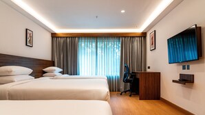 Habitación de hotel con dos camas, un escritorio, una silla, un televisor y una ventana con cortinas.