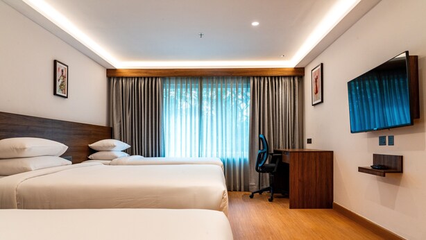 Habitación de hotel con dos camas, un escritorio, una silla, un televisor y una ventana con cortinas.