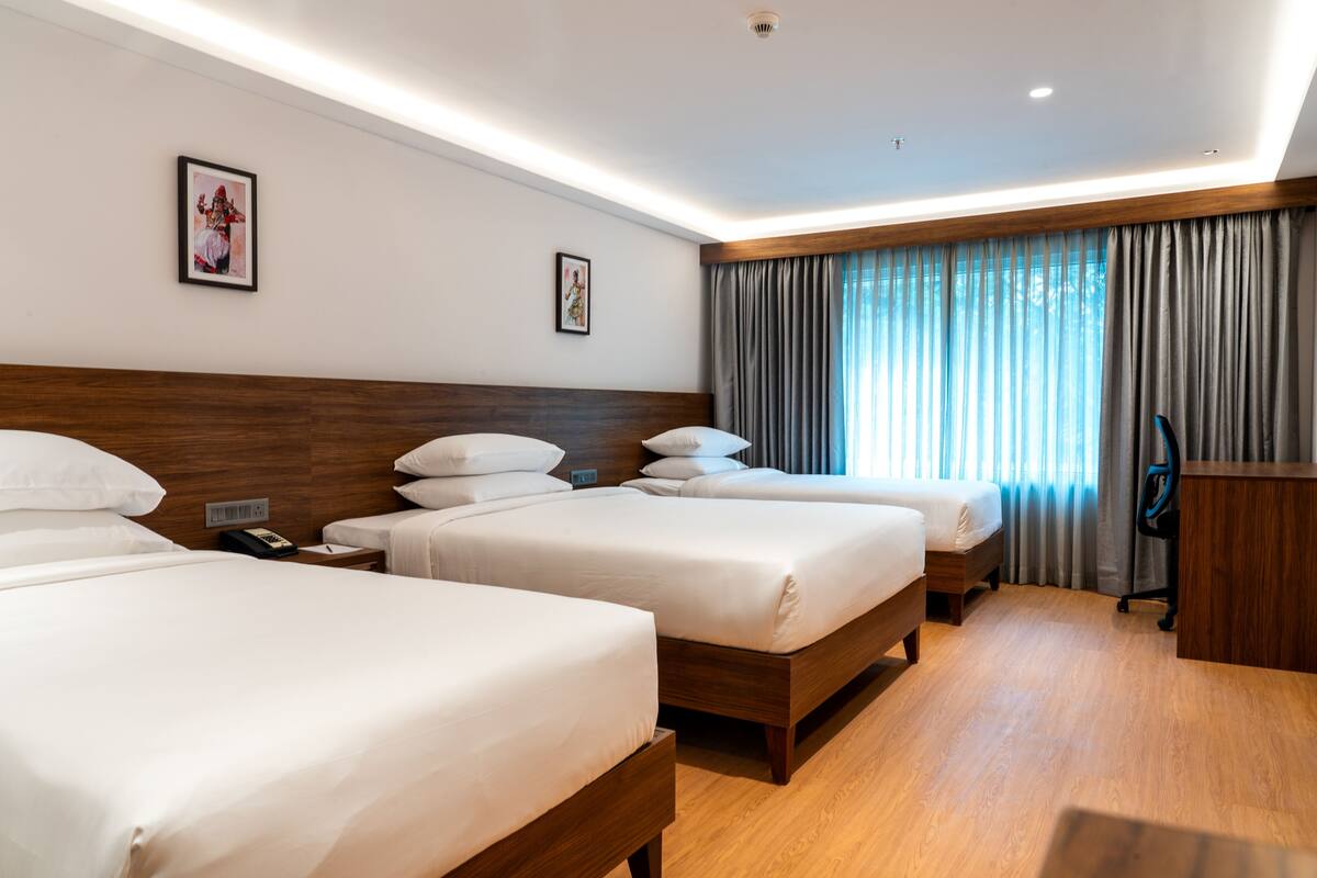 A hotel room with three single beds, a wooden headboard, a desk, and a chair.