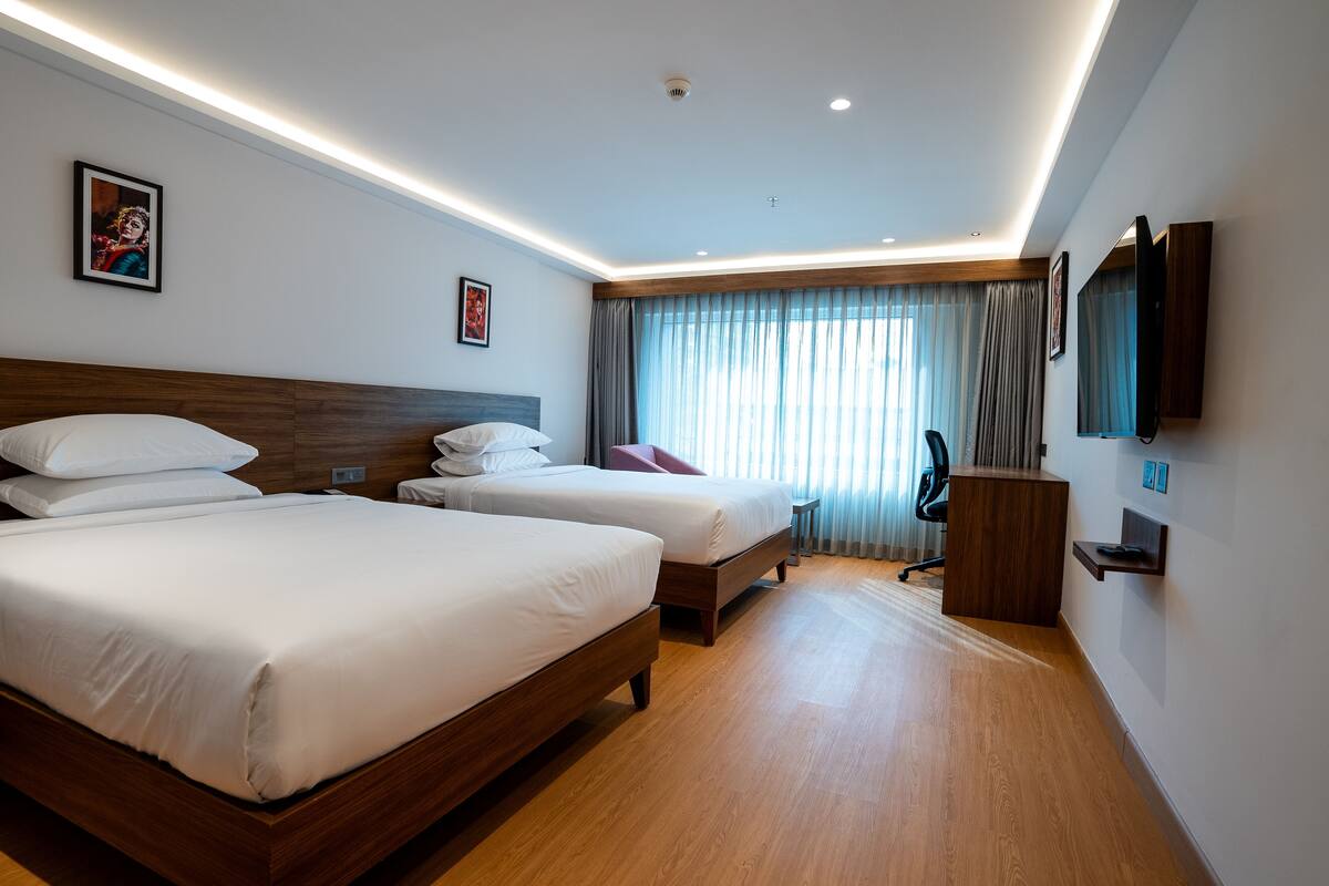 A hotel room with two beds, a desk, a chair, a TV, and a window with curtains.