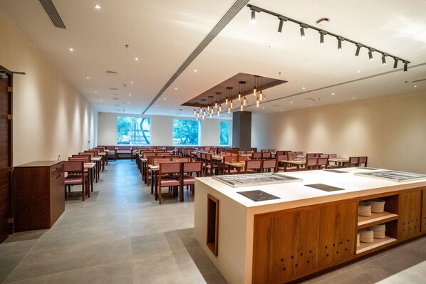 A spacious dining area with multiple tables and chairs, a central island with a sink, and a ceiling with hanging lights. - Rae by Tamara Guruvayur - Formerly Lilac Guruvayur (Chavakkad)