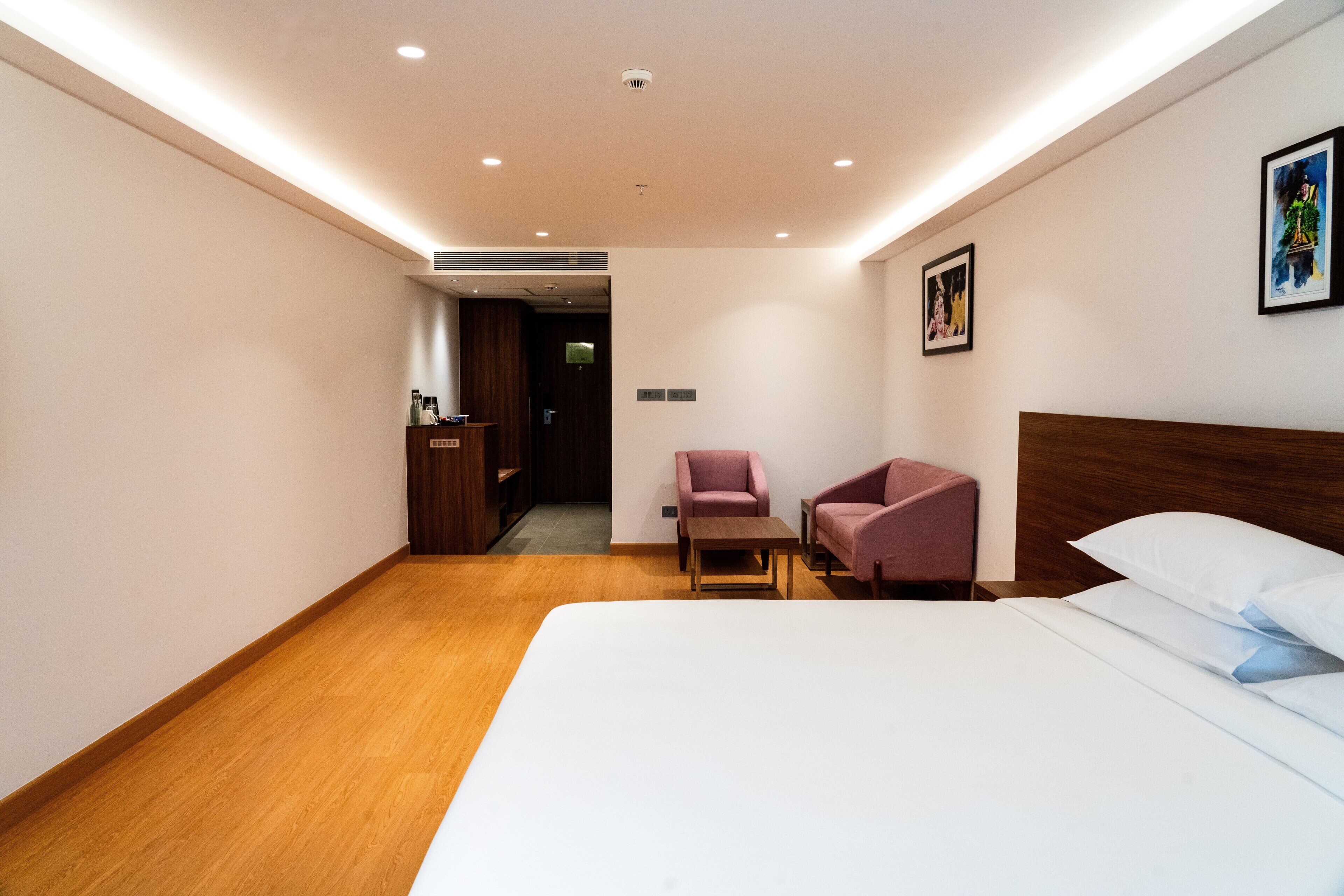 A hotel room with a large bed, a wooden floor, a desk, a chair, and a small table.
