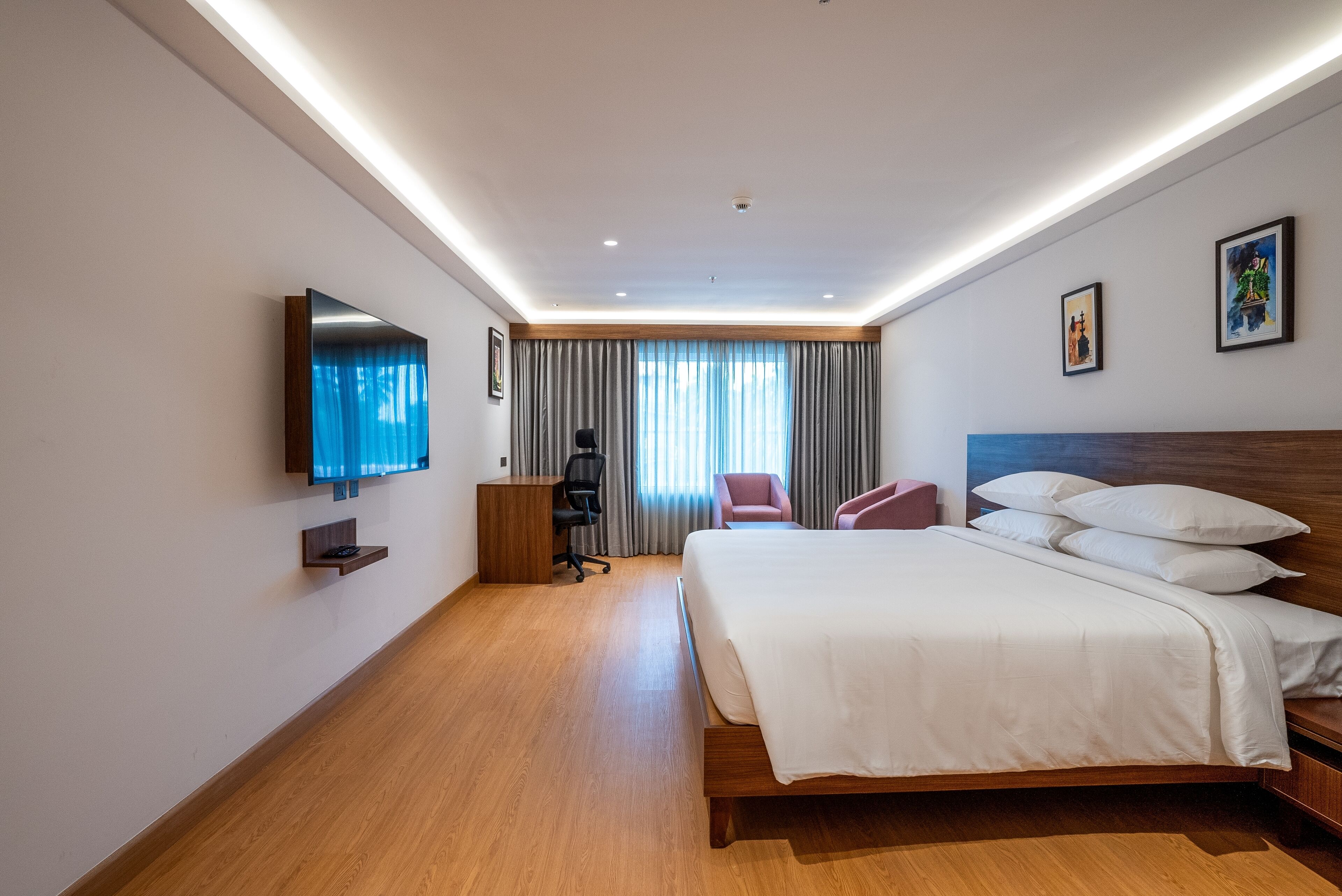 Une chambre d’hôtel moderne, dotée d’un grand lit, d’un bureau, d’une chaise et d’un téléviseur fixé au mur.