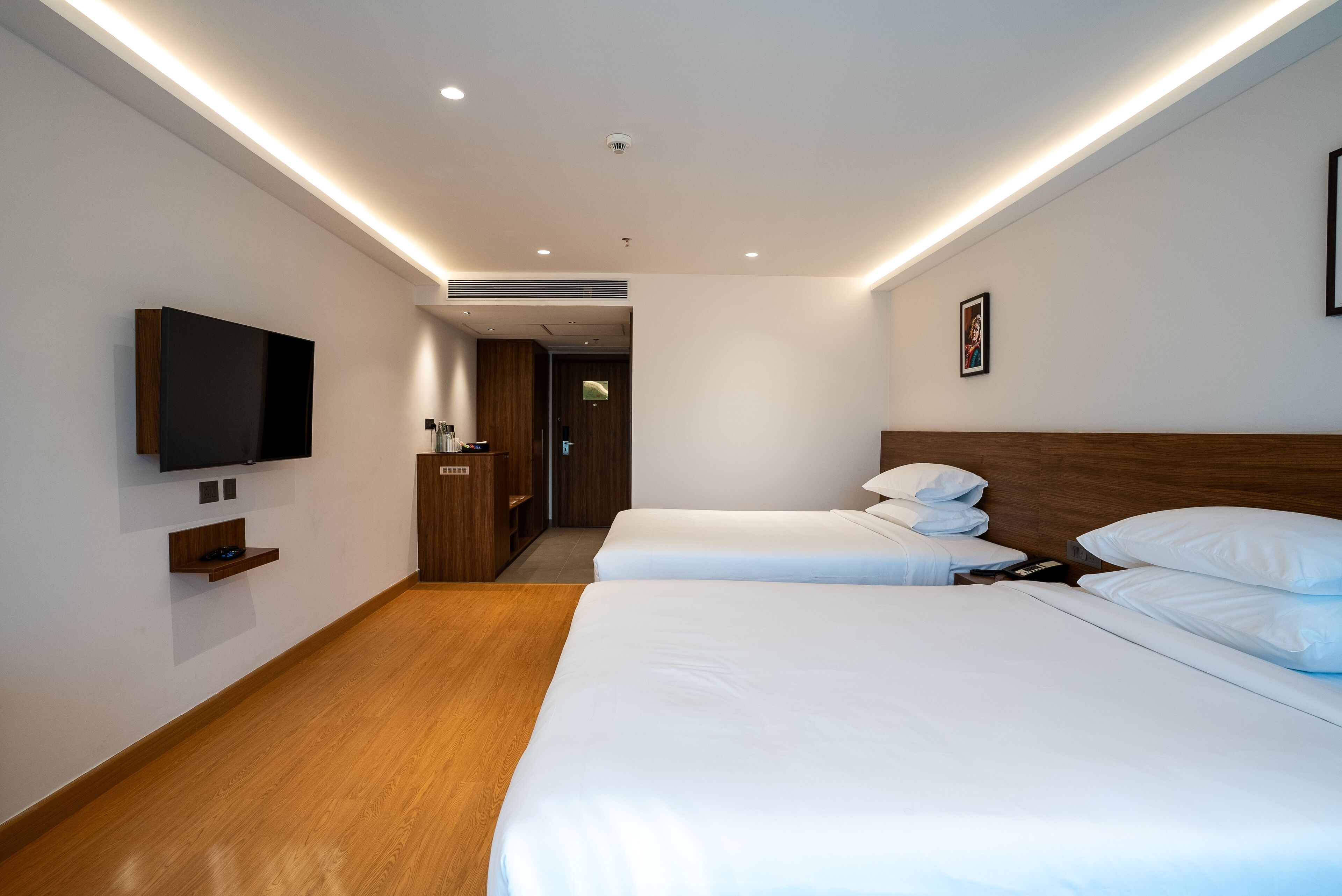 A hotel room with two beds, a flat-screen TV mounted on the wall, and a wooden floor.