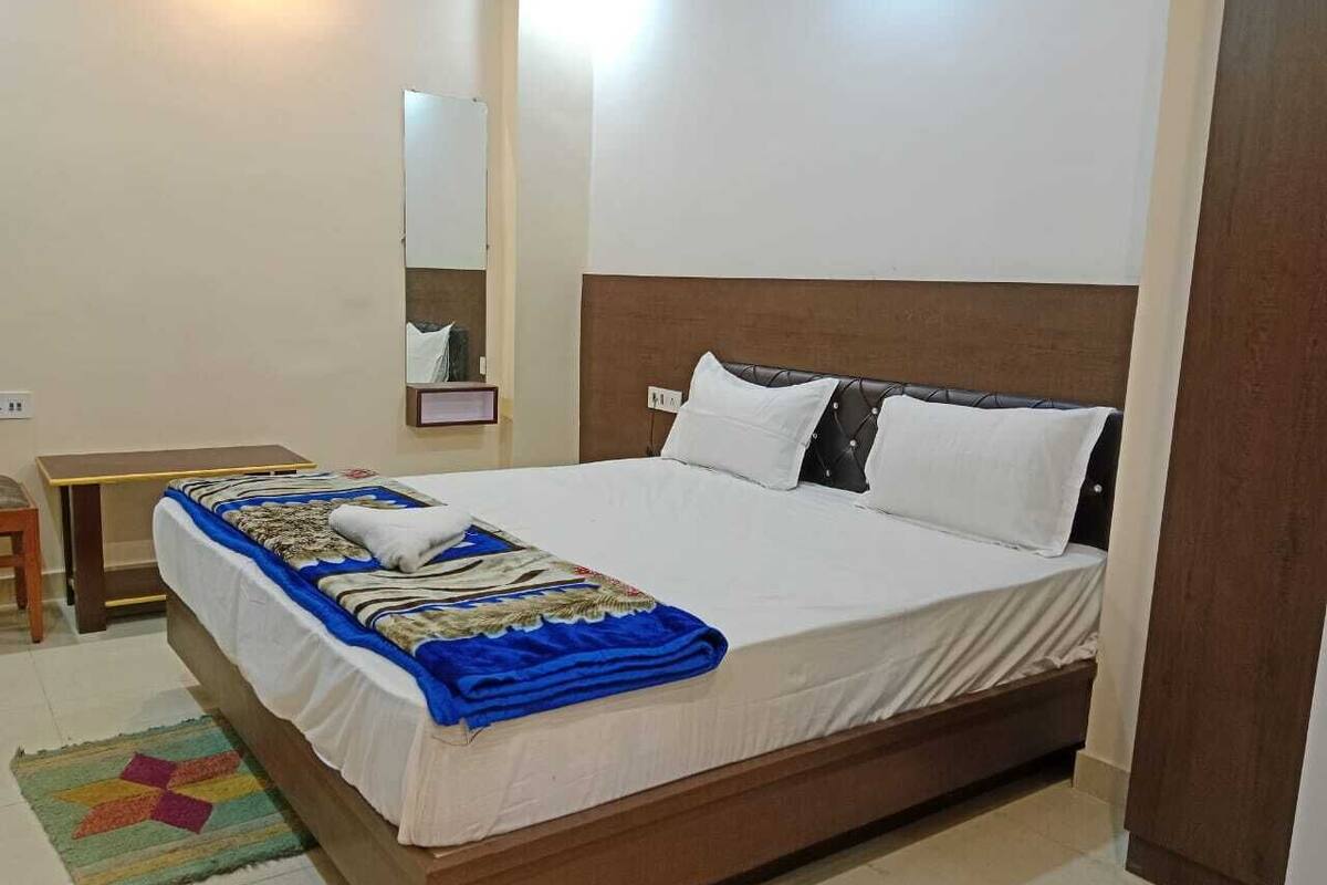 Una cama bien hecha con una colcha blanca y azul, un cabecero de madera y una mesita de noche con una lámpara.