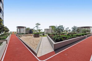 A modern outdoor area with a red running track, landscaped gardens, and cylindrical structures. - Zi apartments - Balcony, Bayview, Sauna, Steam Room & Pool (South Melbourne)