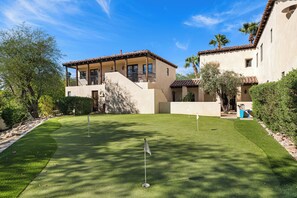 Un terrain de golf bien entretenu, doté d’un green d’entraînement, entouré d’un bâtiment avec un balcon et un espace patio.