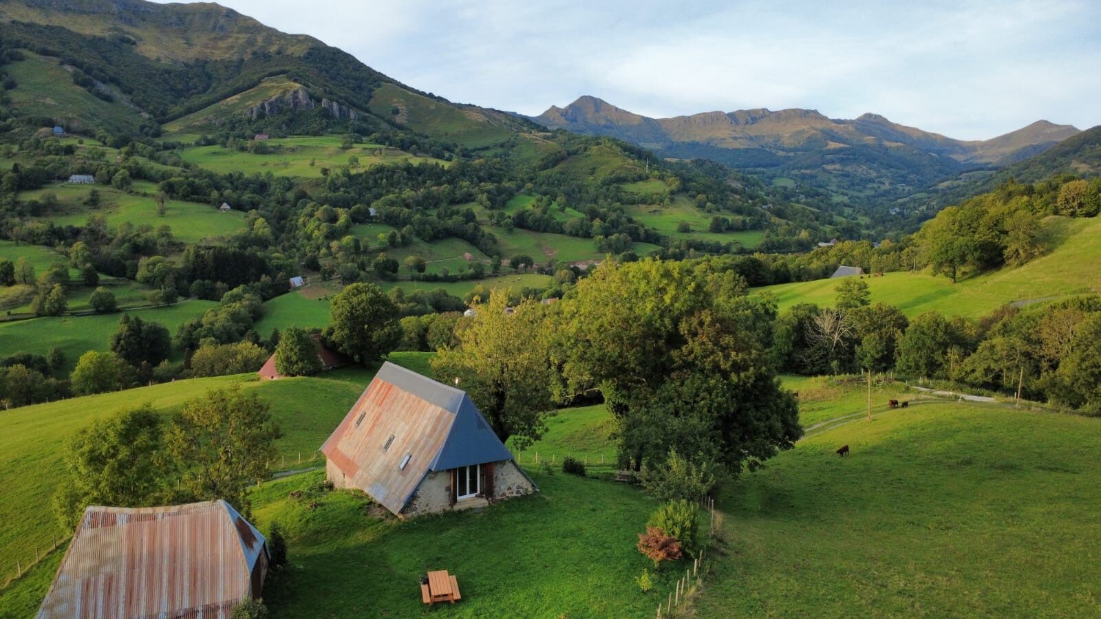A rural landscape with rolling hills, a small house with a sloped roof, and a wooden bench.