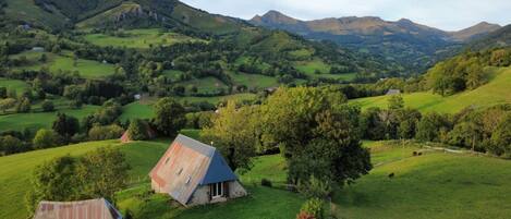 A rural landscape with rolling hills, a small house with a sloped roof, and a wooden bench.