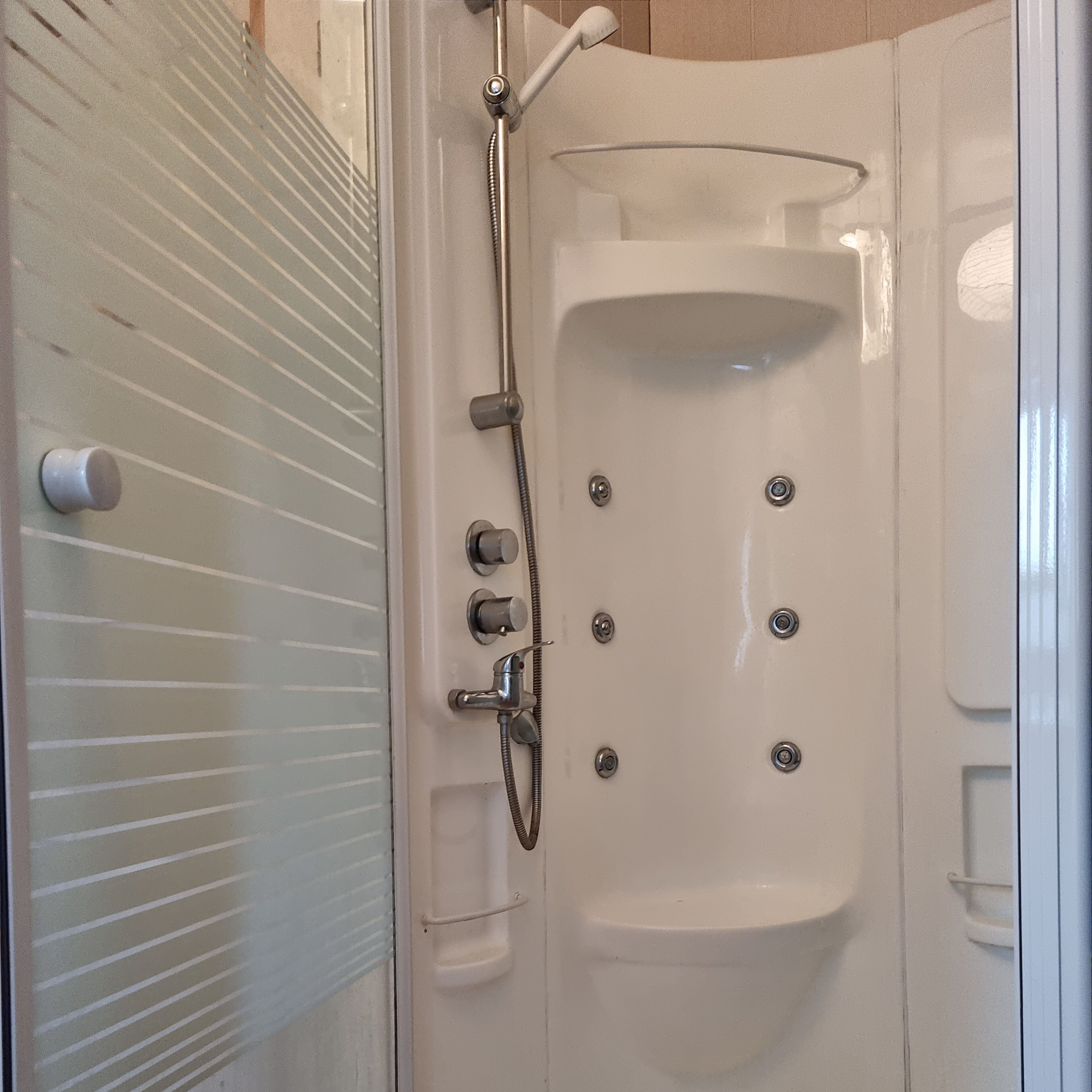 Une baignoire blanche avec un pommeau de douche et des commandes, une porte en verre et un porte-serviettes.