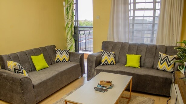 A living room with two grey sofas, each with patterned cushions, a white coffee table, and a view of a balcony with a railing.
