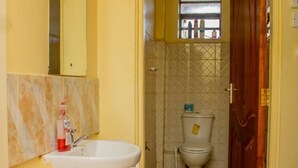 A bathroom with a sink, mirror, toilet, and a pair of blue slippers on a striped mat.