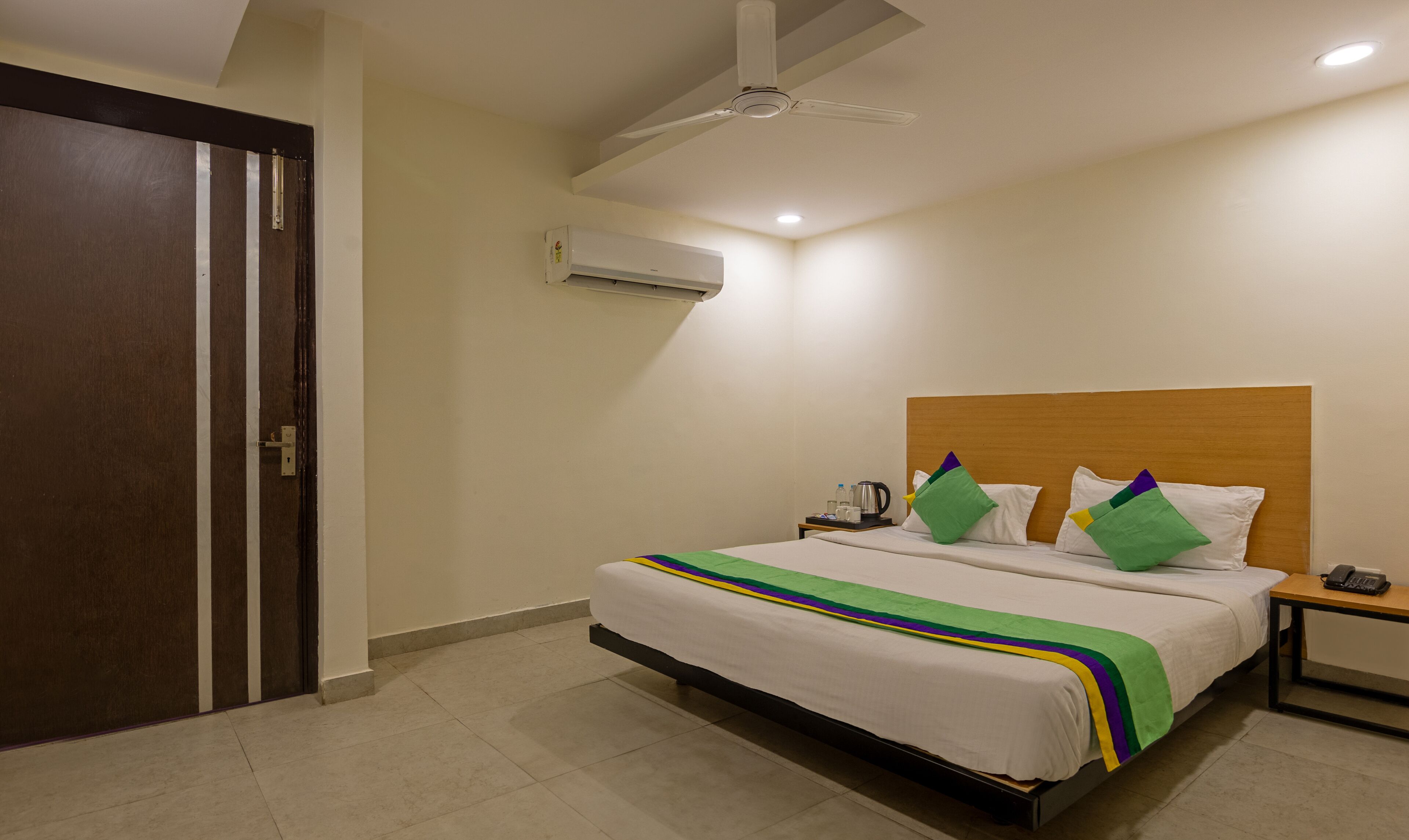 Quarto de hotel com cama, mesa de cabeceira, telefone e ventilador de teto.