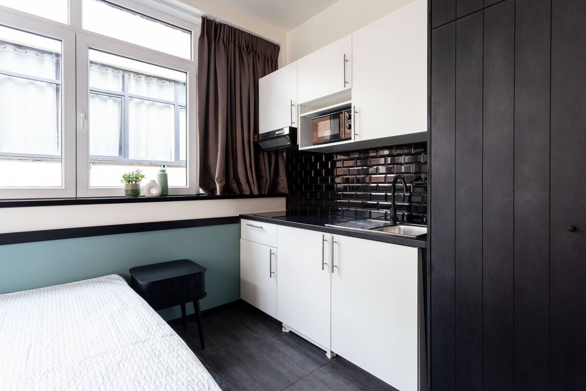 A compact kitchen with white cabinets, a microwave, and a black countertop.