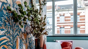 Une pièce avec une table en bois, deux chaises, une plante dans un vase et un mur orné d’un motif.