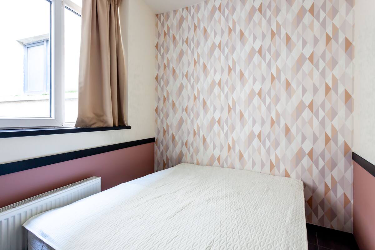 A room with a bed, a window with curtains, and a patterned wall.