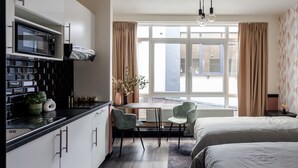 Une chambre d’hôtel moderne dotée d’une kitchenette, de deux lits, d’un coin repas et de grandes fenêtres avec rideaux.
