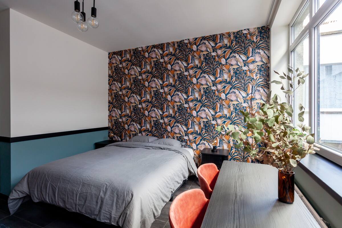 A bedroom with two beds, a large window, and a floral wallpaper.