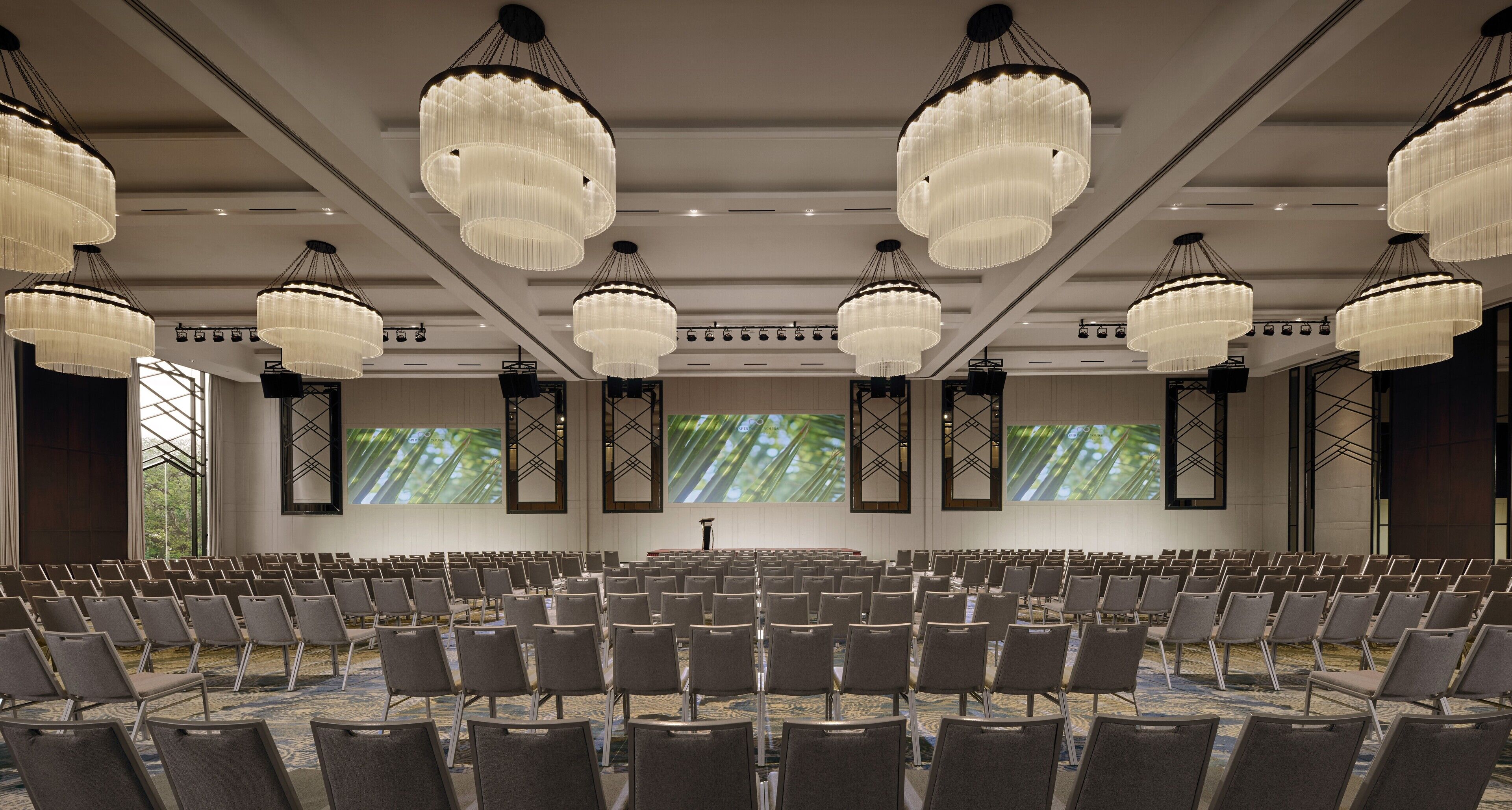 Une salle de conférence avec des rangées de chaises, de grands lustres et un pupitre.