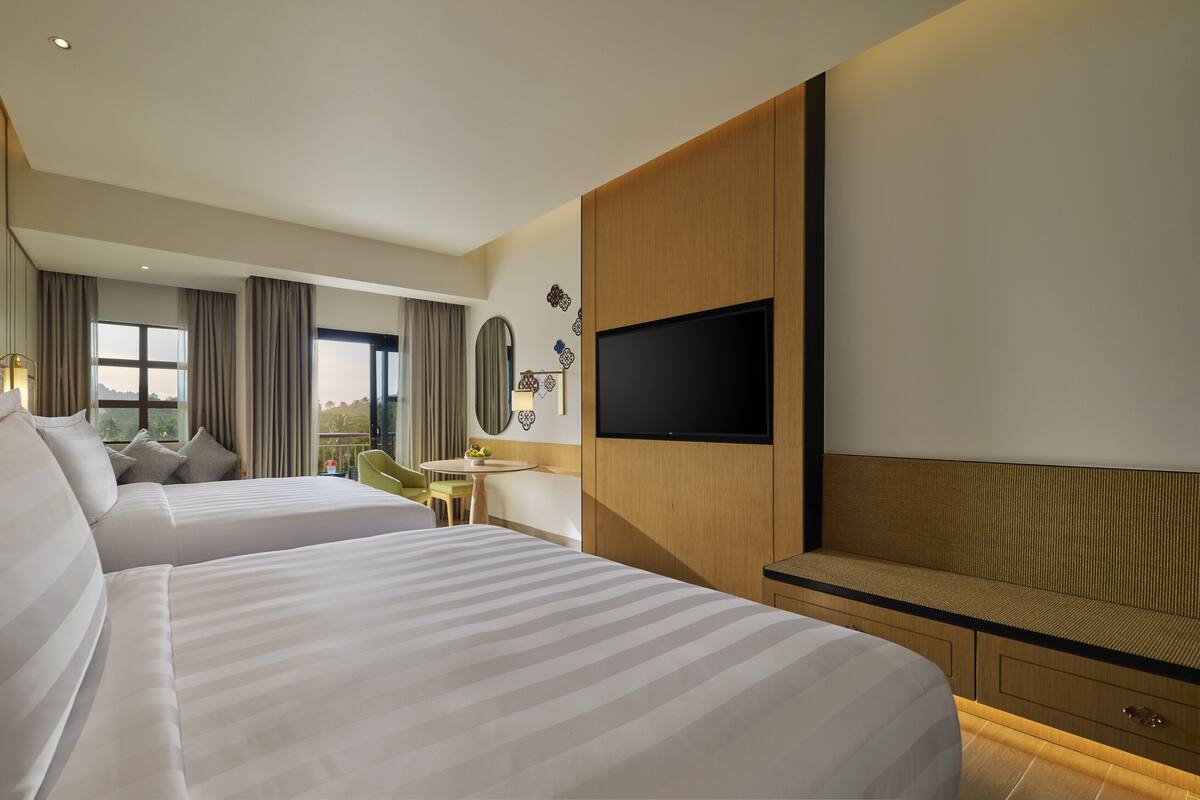 Een hotelkamer met twee bedden, een televisie, een bureau en uitzicht op het omliggende landschap.