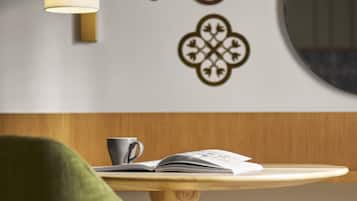 Eine Wand mit dekorativen Mustern, eine Lampe, ein Tisch mit einem Buch und einer Tasse sowie ein grüner Sessel.